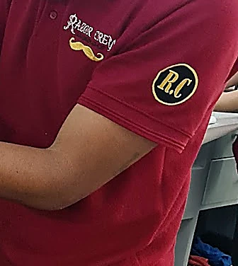 Polo guinda del uniforme con Razor Crew y un bigote dorado bordados, y el parche R.C. en la manga
