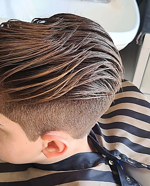 Cabello largo peinado hacia atrás con fade en la nuca, sobre la capa a rayas negro y arena